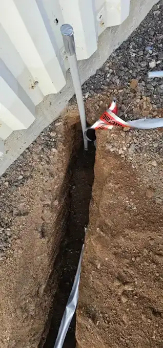 Conduit stub-up at the building line, marked with electrical warning tape.