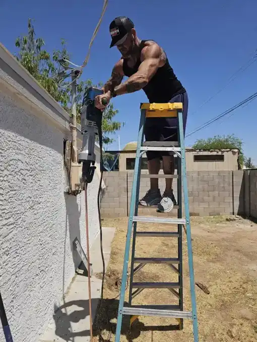 Before — driving the new ground rod, with the original meter/breaker panel still on the wall.